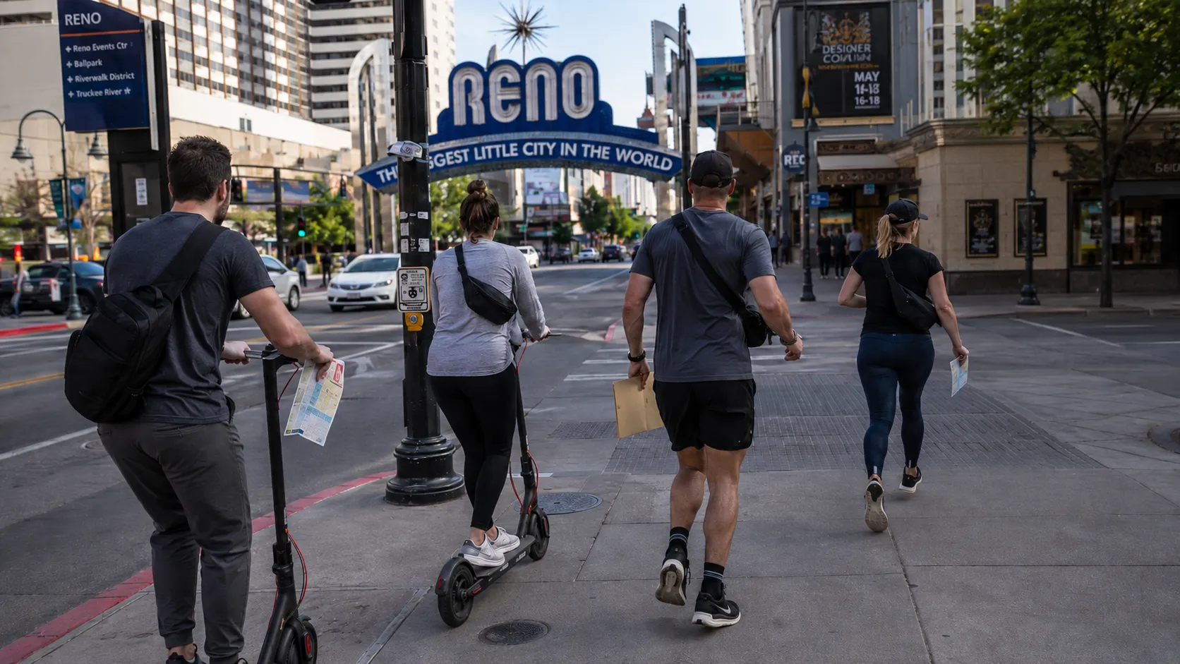 Executives with scooters and maps crossing a downtown Reno street under the Reno arch.